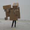 imagette montrant l'trage assemblage des jambes d'un homme supportant un amas de botes en carton, en guise de corps et de tte.